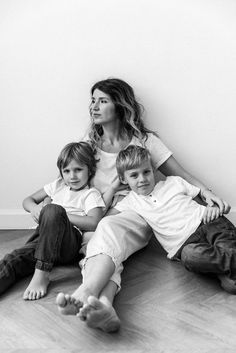 a woman and two children sitting on the floor in front of a wall with their feet up