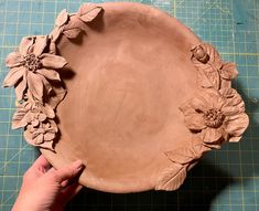 a person is holding a clay plate with flowers on it