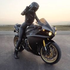 a person sitting on a black motorcycle in the middle of an empty parking lot at sunset