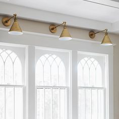 three lights are hanging from the ceiling in front of two windows with arched glass panes