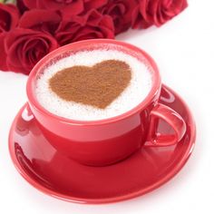 a cup of coffee with a heart on it and some red roses in the background