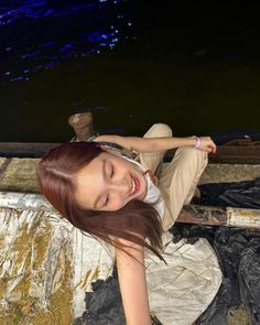 a woman laying on top of a tarp next to a body of water at night