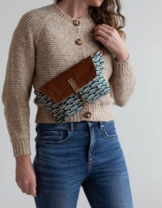 a woman in jeans and a sweater holding a brown purse with an interesting design on it