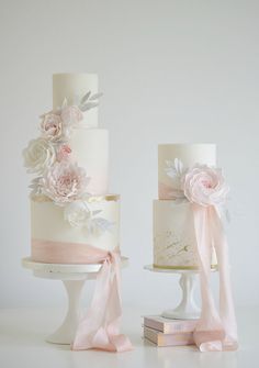 two tiered wedding cakes with pink flowers and ribbons on them, one is white and the other is light pink