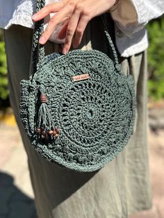 a woman holding a green crocheted bag with tassels on the handles