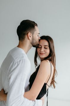 a man and woman embracing each other in front of a white wall