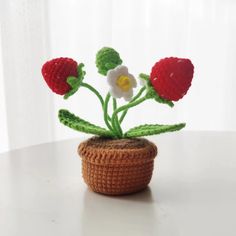 a small crocheted flower pot with three flowers in it sitting on a table