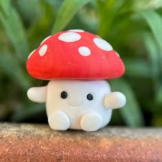 a small white and red mushroom sitting on top of a wooden table next to green plants