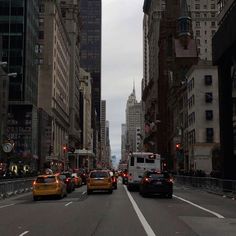 several cars driving down a city street with tall buildings in the background and traffic lights on both sides