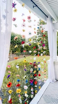 an outdoor area with white curtains and colorful flowers hanging from the side of the building