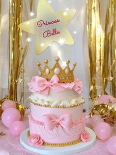 a pink and gold princess cake with a tiara on top, surrounded by balloons