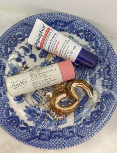 a blue and white plate topped with items like lipstick, toothpaste and scissors