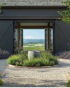 an open barn door leading into a lush green field with purple flowers and lavenders