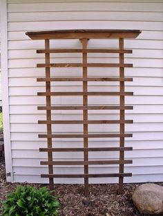 a wooden trellis on the side of a house next to a rock and planter