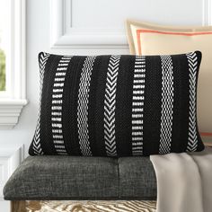 a black and white pillow sitting on top of a gray couch next to a window