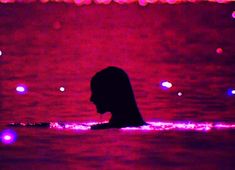 a person is swimming in the water at night with colorful lights on it's surface