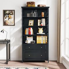 a black bookcase with many books on it in front of a desk and window