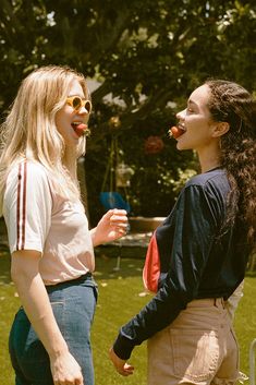 two young women standing next to each other in the grass