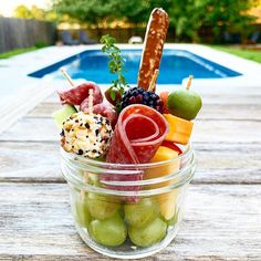 a glass bowl filled with assorted fruits and meats next to a swimming pool