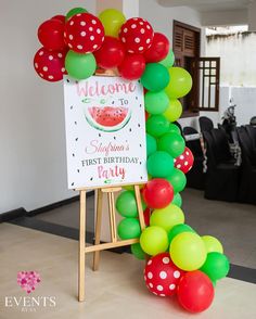 a welcome sign and balloon arch for a watermelon themed first birthday party with polka dots