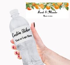 a hand holding a water bottle with the label custom sticker next to an orange tree