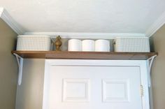 a white door with some baskets on the shelf above it and two rolls of toilet paper