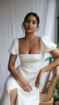 a woman in a white dress sitting on a chair with her hands on her hips