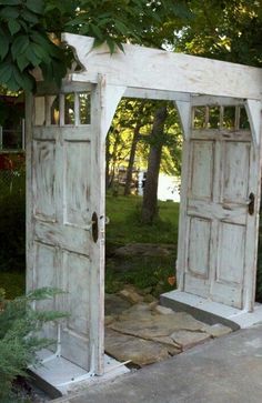 an old white wooden gate with two doors open in the middle of a garden area