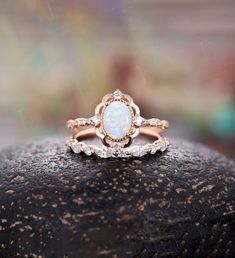 a close up of a ring with a rainbow colored stone in the center on top of a rock