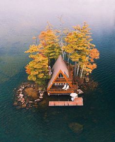 an aerial view of a house on the water with trees in fall colors around it