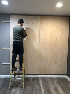 a man on a ladder painting the walls in a room with wood floors and gray walls