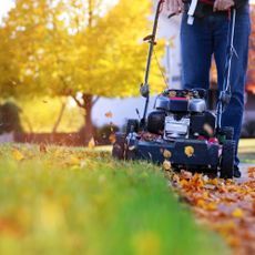 a woman is mowing the grass with her lawnmower in fall time,