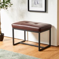 a brown leather bench sitting on top of a wooden floor next to a potted plant