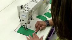 a woman is using a sewing machine to sew on green paper with her hands