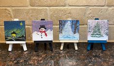 four small easels with paintings on them sitting in front of a brick wall