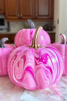 three pink marbled pumpkins sitting on top of a white countertop in a kitchen