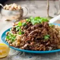 a blue plate topped with meat and rice next to lemon wedges on a table