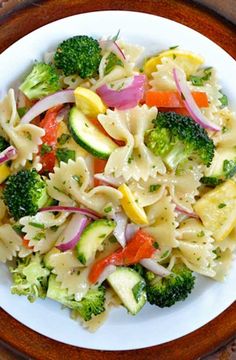 a white plate topped with pasta and veggies on top of a wooden table