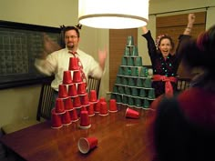 a man and woman standing in front of a christmas tree made out of plastic cups