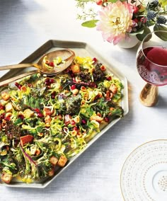 a white plate topped with a salad next to a glass of wine and a cup