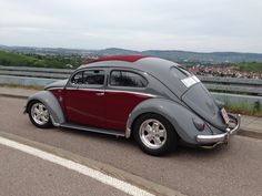 an old vw bug is parked on the side of the road with mountains in the background