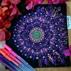 some markers and pens are sitting on a table next to a drawing book with an intricate design