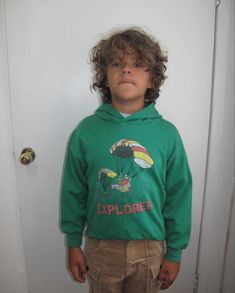 a young boy standing in front of a door wearing a green sweatshirt and tan pants