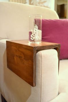 a small wooden table sitting on top of a white couch next to a pink pillow