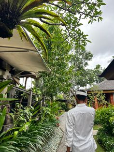 a man walking down a sidewalk next to lush green plants