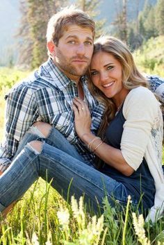 a man and woman are sitting in the grass with their arms around each other, smiling