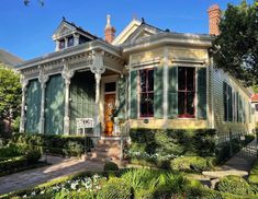 an old victorian house with green shutters and red trim on the front door is surrounded by greenery