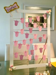 a baby's clothes line with pink ones hanging from it and flowers on the table