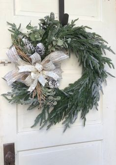 a wreath hanging on the front door with pine cones and evergreens attached to it