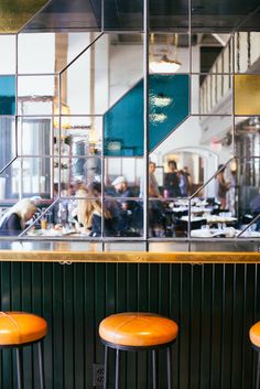 three orange stools in front of a bar with mirrors on the wall and people eating